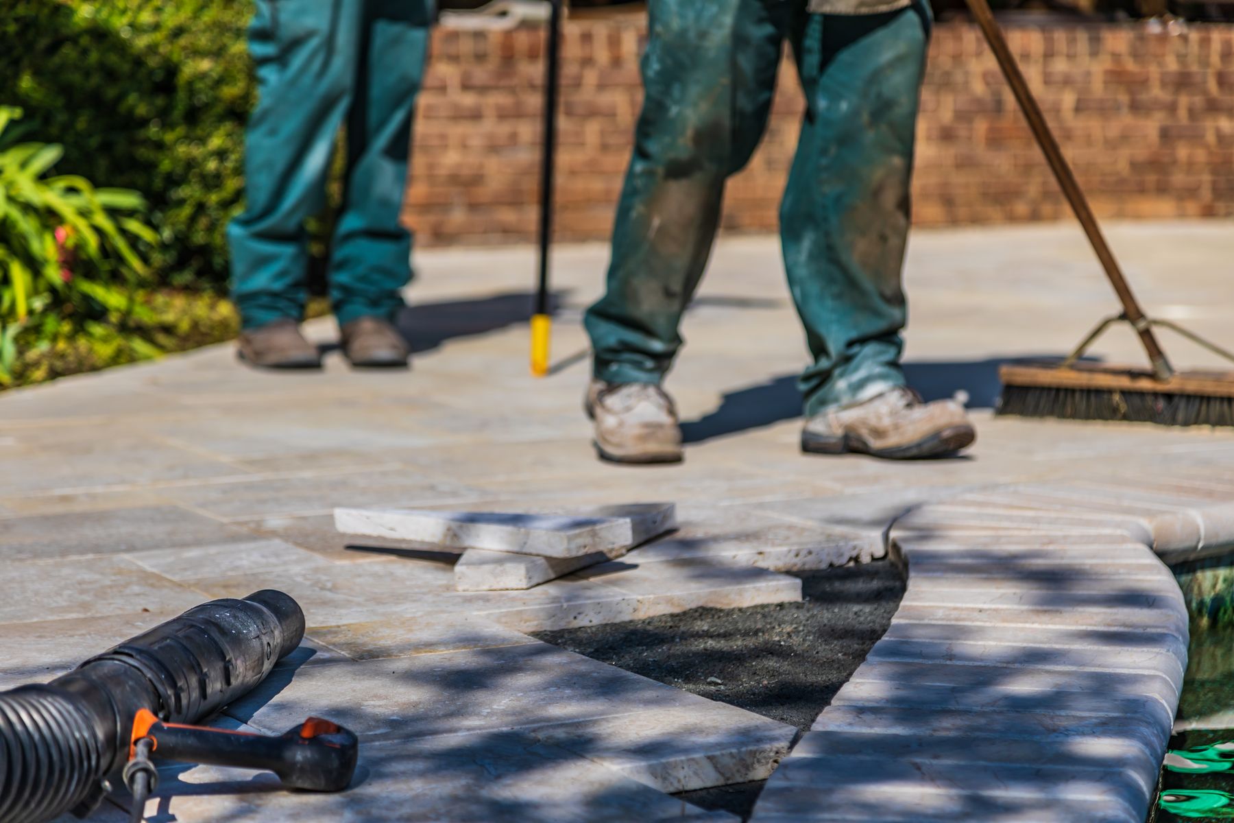 Workers setting stone tiles on an outdoor patio beside a brick wall